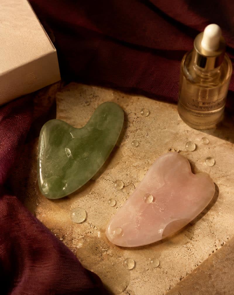 Gua sha stones and facial serum on travertine